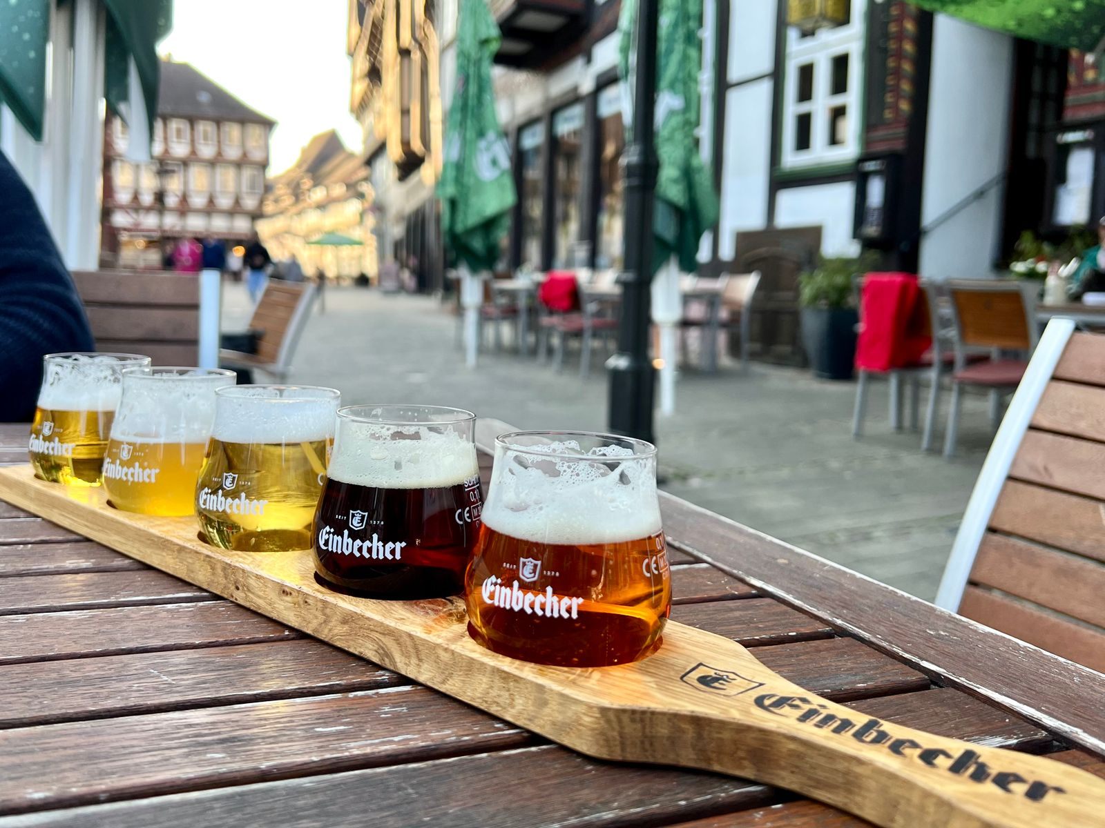 Tasting flight of German beers on a wooden paddle at an outdoor table in a half-timbered town