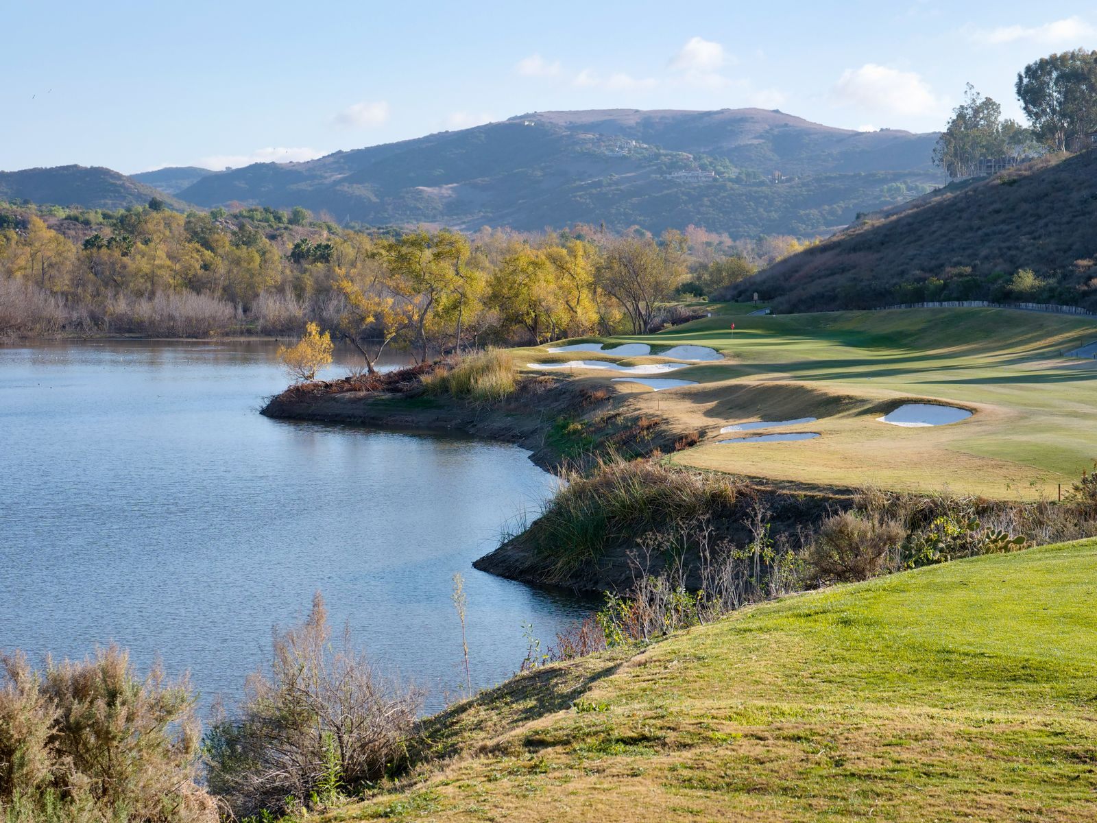 Golf course curving around a calm lake with wooded hills behind