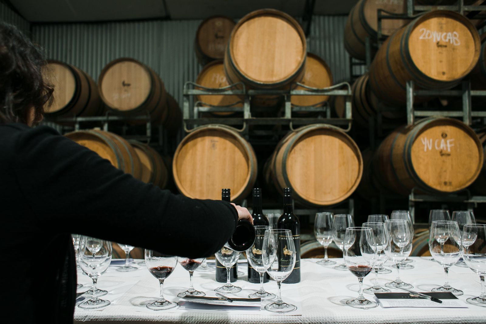 Sommelier pouring wine at a tasting table in front of oak barrels